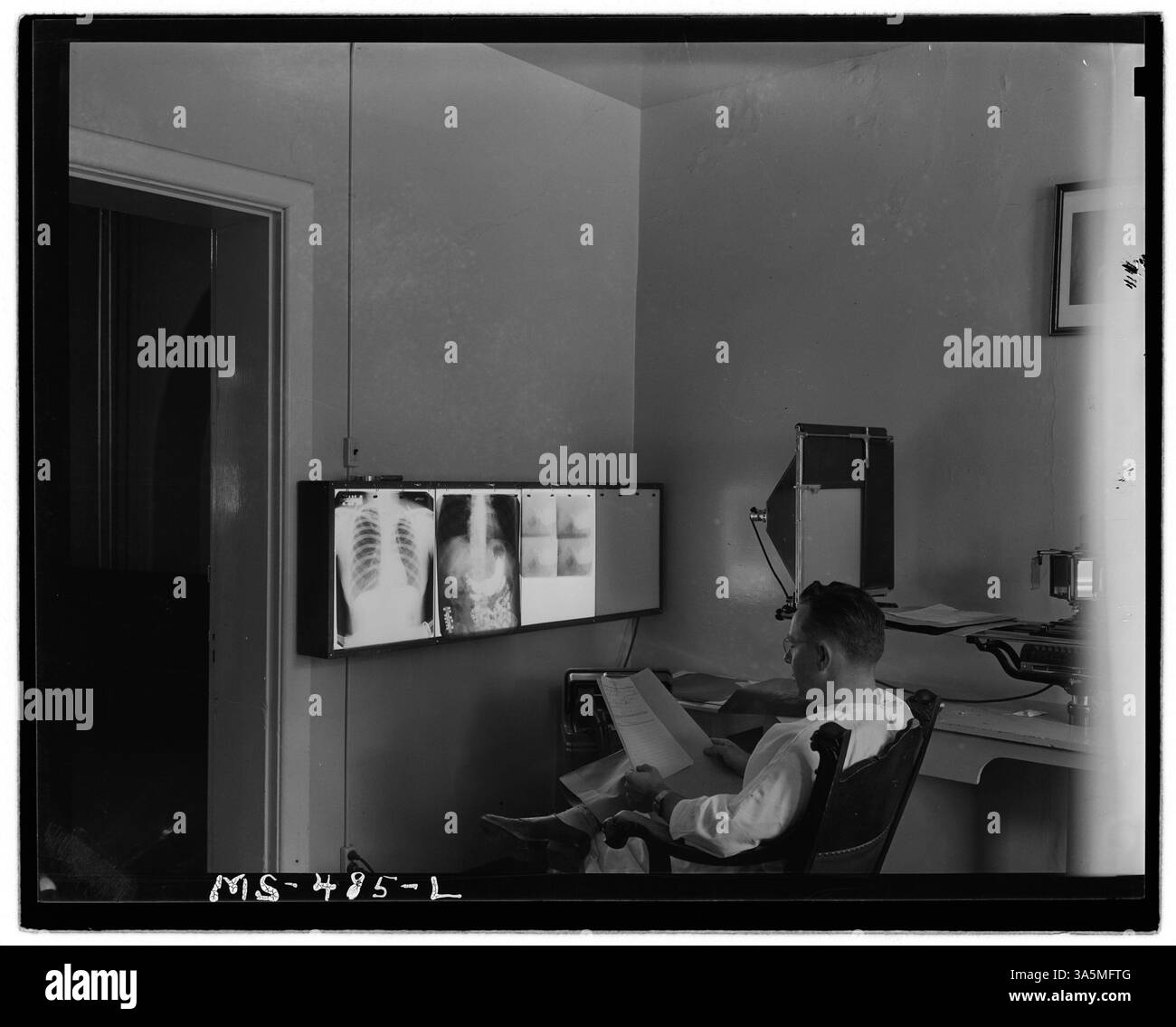 Un medico aziendale esamina i raggi X e la storia del caso di un paziente presso l'ospedale aziendale della Colorado Fuel & Iron Company a Pueblo, Colorado. Questa immagine evidenzia l'assistenza sanitaria fornita ai lavoratori in ambienti industriali. Foto Stock