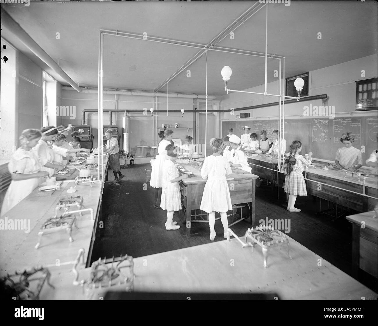 Gli studenti sono ritratti cucinare nella Domestic Science Classroom della Calhoun School. Una ricetta per l'insalata di banane e noci è scritta sulla lavagna, sottolineando l'educazione culinaria pratica. Foto Stock