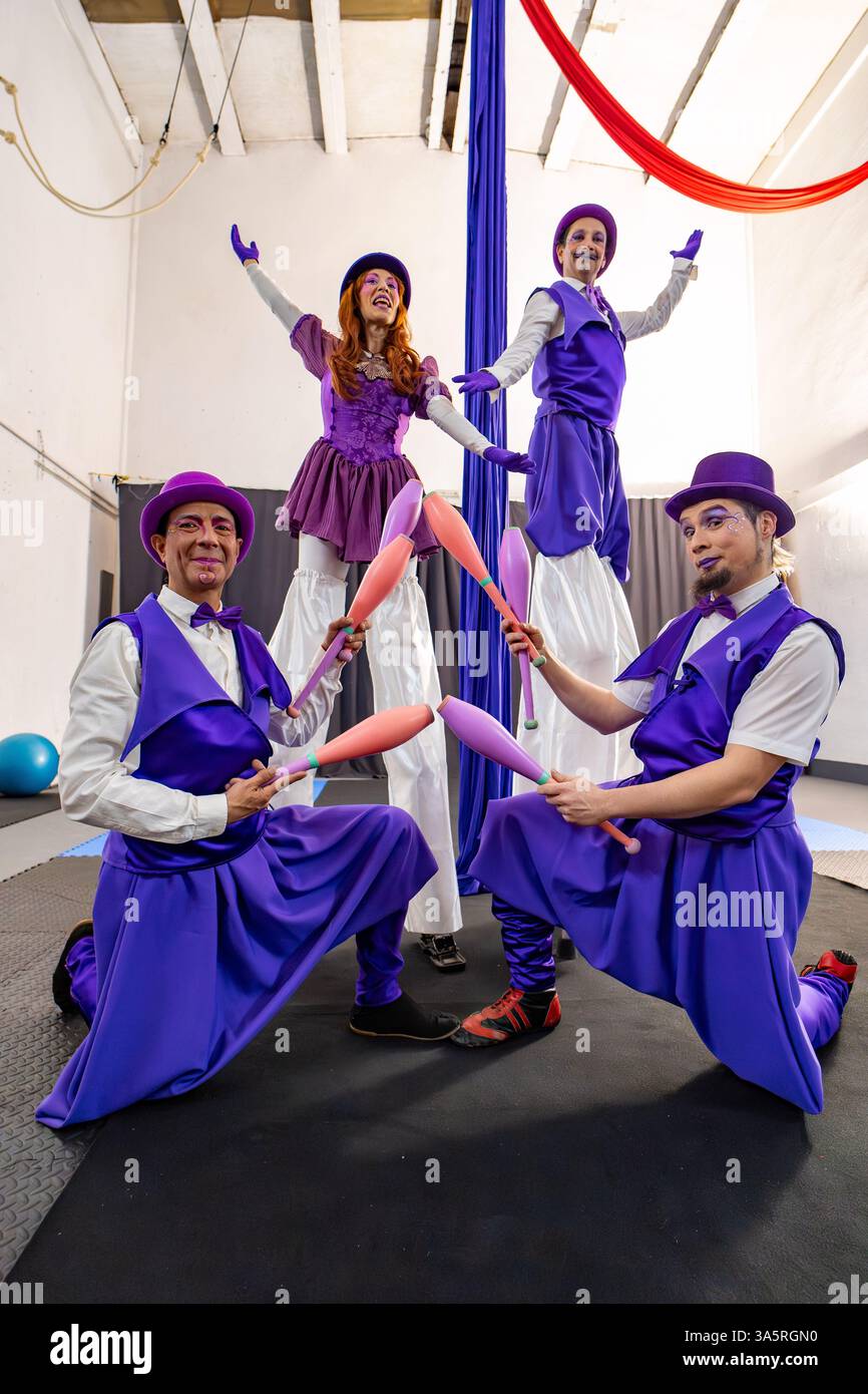 Quattro artisti circensi in vivaci costumi viola mostrano le loro abilità di giocoliere e di camminare su palafitte all'interno di una palestra di allenamento Foto Stock Quattro artisti circensi in vivaci costumi viola mostrano le loro abilità di giocoliere e di camminare su palafitte all'interno di una palestra di allenamento Foto Stock