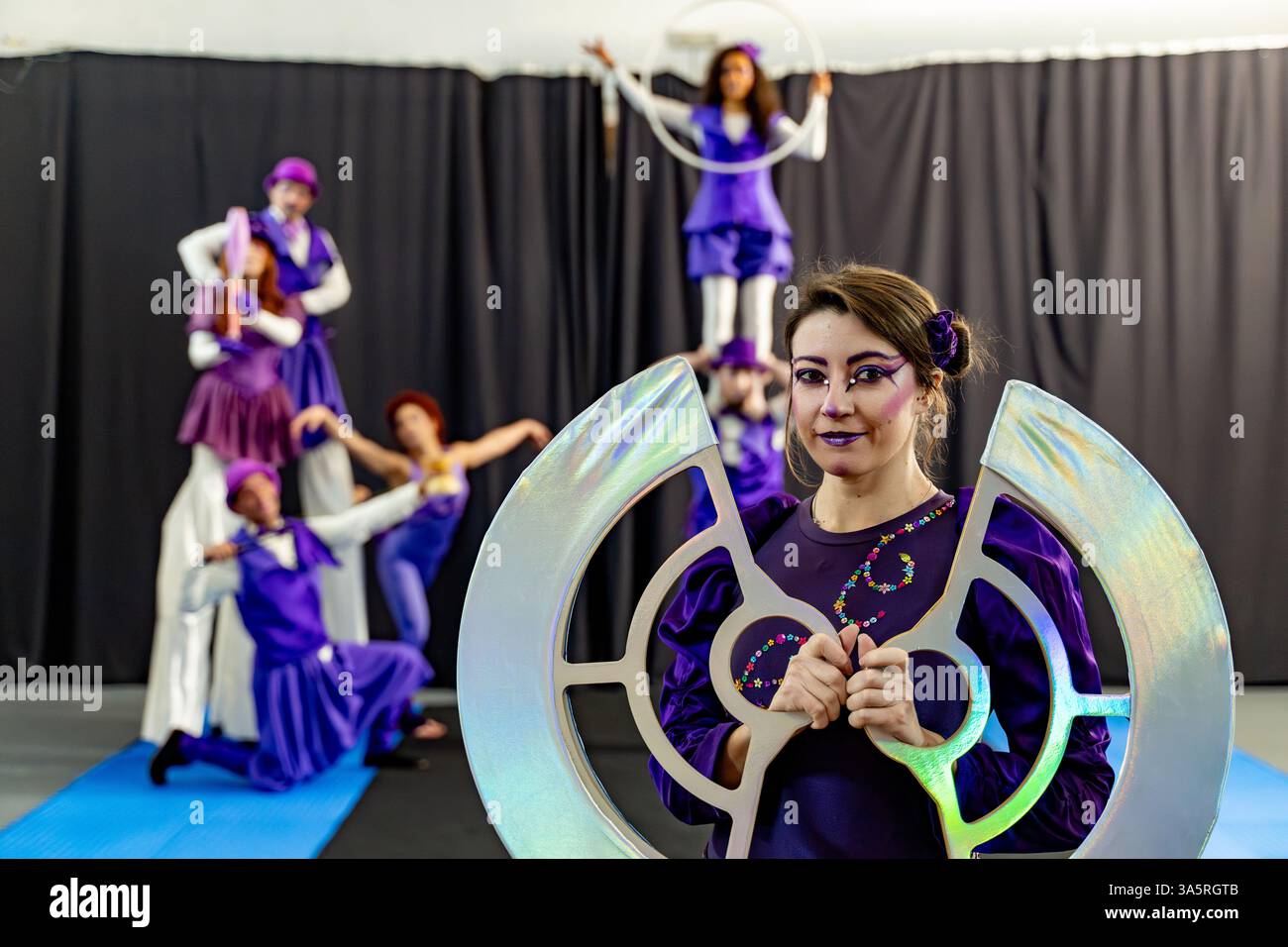 Gli artisti del circo in costumi viola provano camminate su palafitte, acrobazie e hula hooping, con un'attrezzatura iridescente in primo piano Foto Stock Gli artisti del circo in costumi viola provano camminate su palafitte, acrobazie e hula hooping, con un'attrezzatura iridescente in primo piano Foto Stock