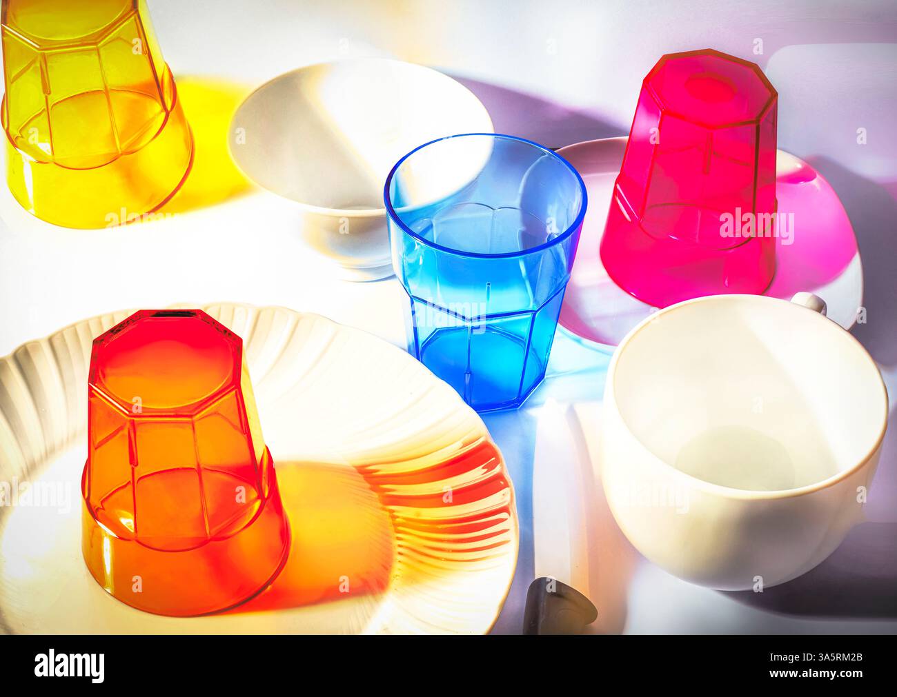 Bicchieri in plastica colorati con piastre e ciotole di colore chiaro Foto Stock