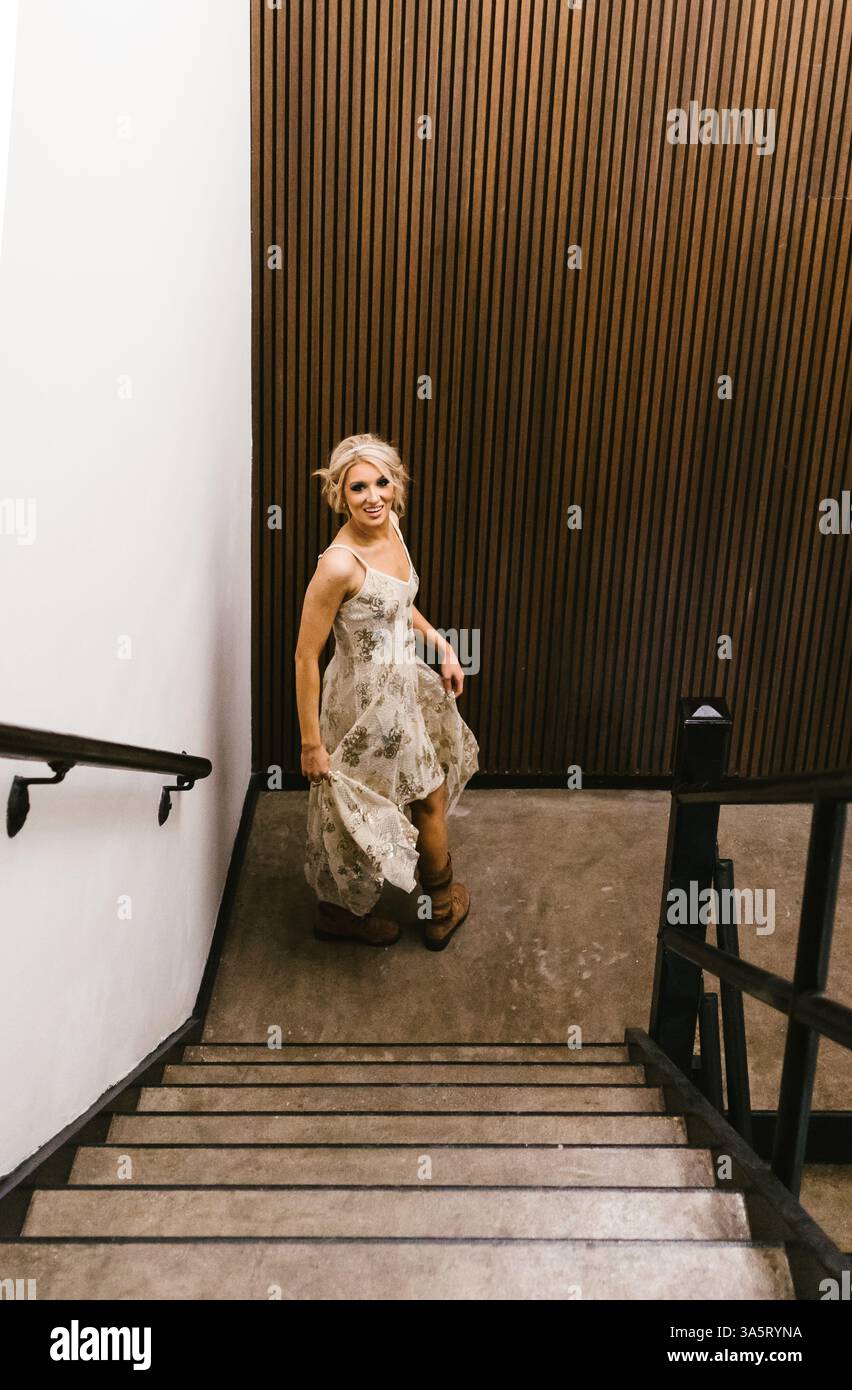 La donna in abito floreale sorride e gira modellando in un edificio rustico Foto Stock