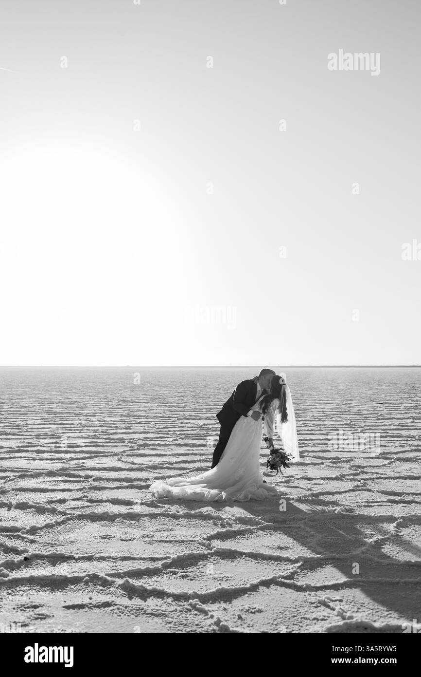 Sposa e sposo bianco e nero di classe da sogno che si baciano sulle saline Foto Stock