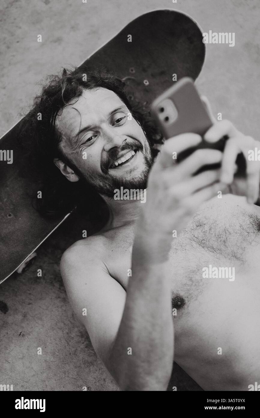 Uomo che utilizza smart phone mentre giaceva sul sedile a skate park Foto Stock