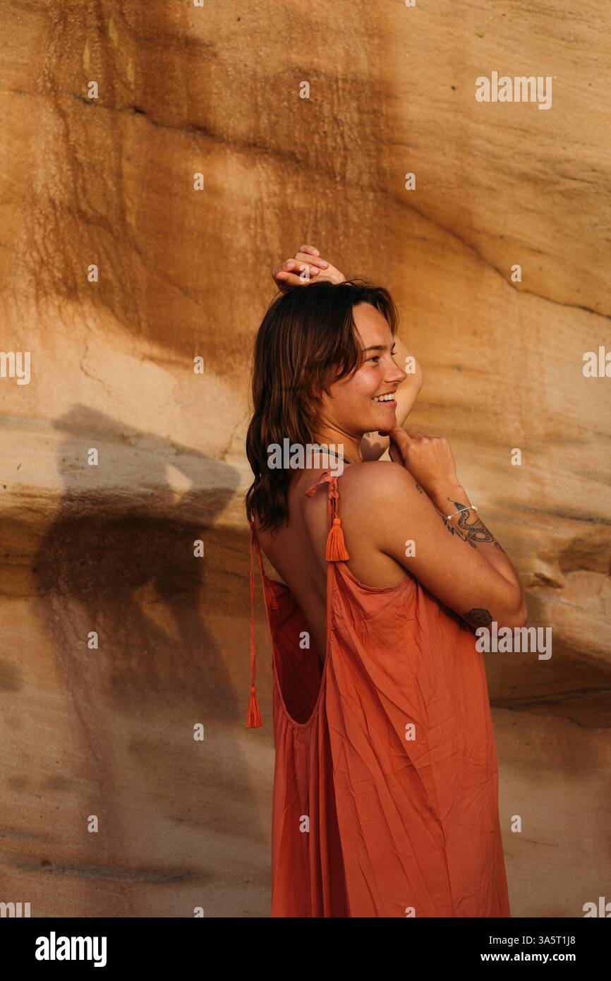 Donna sorridente con le braccia sollevate alla luce calda del sole davanti a un re Foto Stock