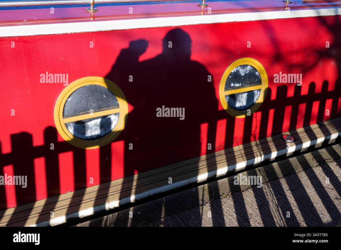 La mia ombra su una casa galleggiante ormeggiata sul Tamigi da Sandford Lock. L'area intorno a Sandford Lock Over the Tamigi è un luogo molto apprezzato da chi pratica jogging, escursionisti, appassionati di cani e molti altri che frequentano le fantastiche passeggiate in questa zona. Un nuovo panettiere artigianale che offre pane a pasta madre di prima qualità è ora un'attrazione locale... Qui vediamo ombre di me e una recinzione su una casa galleggiante ormeggiata appena a monte della chiusa, presto in una bella giornata d'inverno. Sto andando a prendere il pane, allora è la colazione domenicale ordinata. Foto Stock