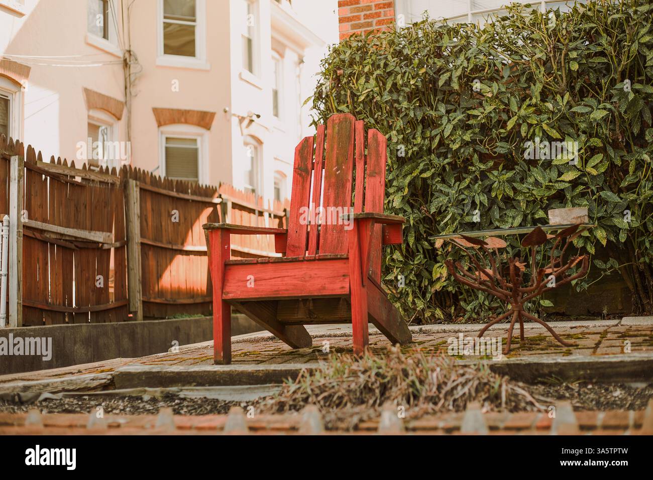 Una sedia rossa sullo sfondo con uno sfondo di verde e una recinzione in legno a Philadelphia, Pennsylvania, USA, il 23 marzo 2025 Foto Stock