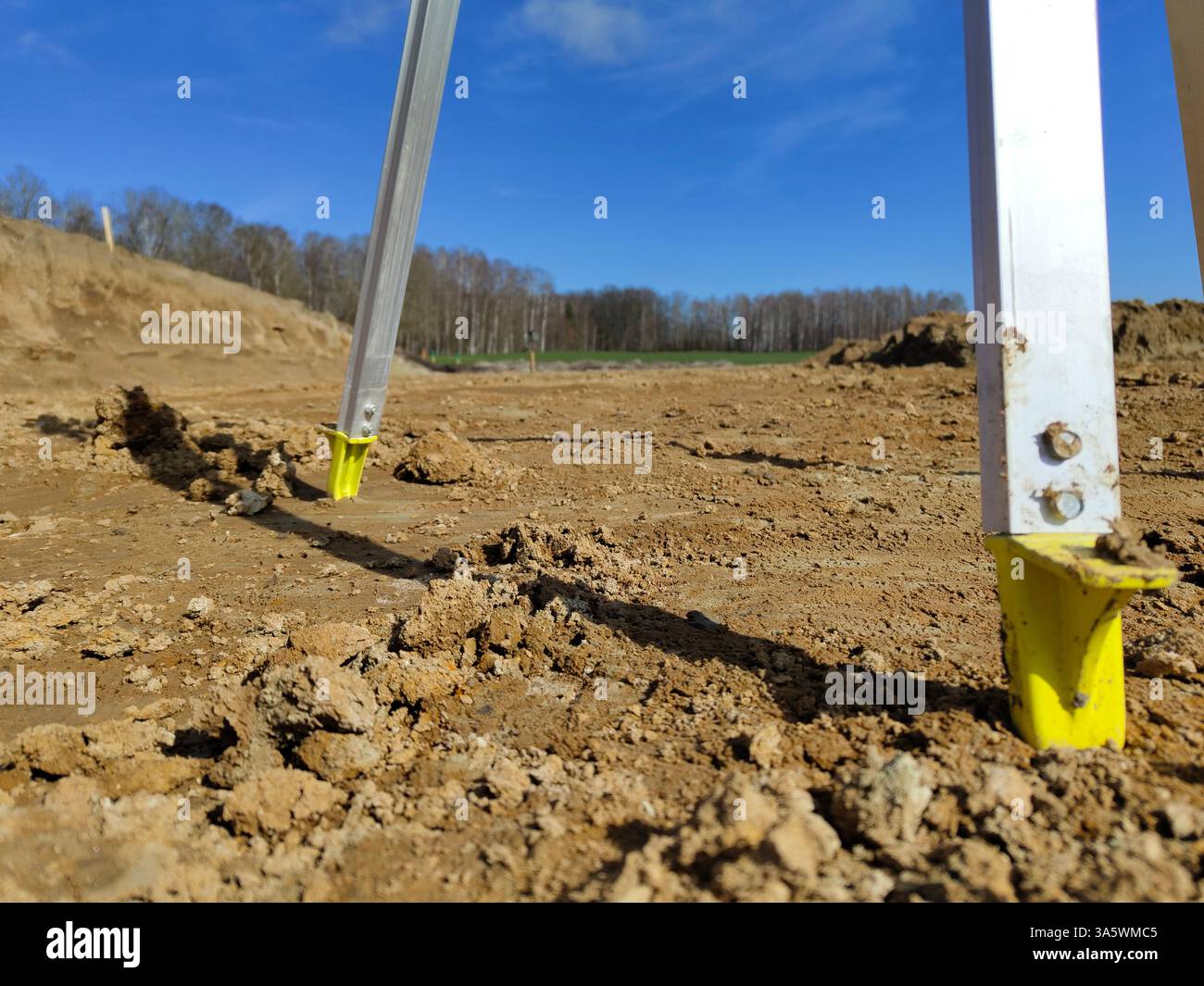 Strumenti di misurazione per costruzioni in un campo rurale fangoso con cielo azzurro e alberi. Foto Stock