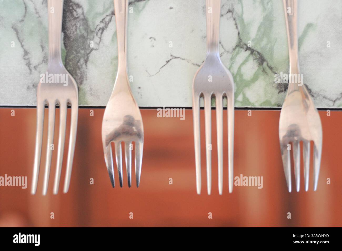 Quattro forcelle in acciaio inox su marmo con sottili riflessi sotto un'illuminazione soffusa Foto Stock
