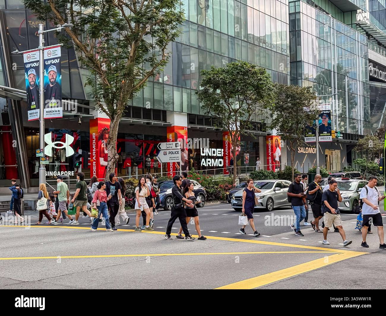 Orchard Road a Singapore con persone che attraversano la strada di fronte ai centri commerciali. Foto Stock