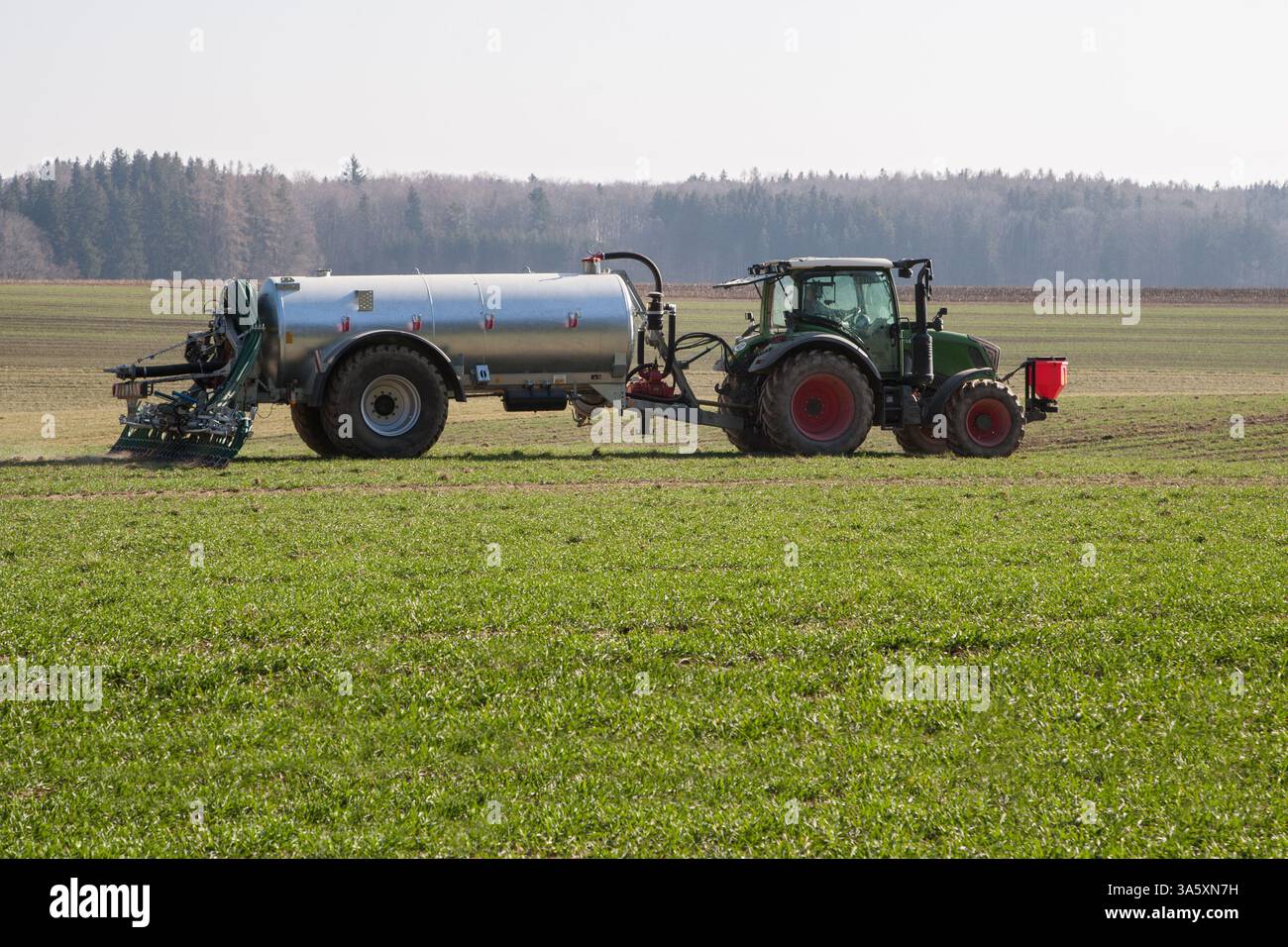 Un trattore con un moderno spandiconcime distribuisce i liquami sul campo. Un'eccessiva fertilizzazione inquina le acque sotterranee con nitrati. Foto Stock