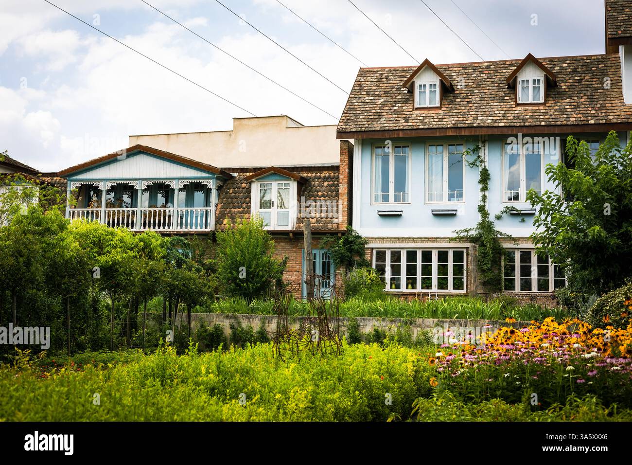 Pittoresco cottage di campagna con pareti blu, tetto in piastrelle rustiche, vegetazione lussureggiante e un'affascinante serra. Perfetto per i temi della vita rurale, architetto Foto Stock Pittoresco cottage di campagna con pareti blu, tetto in piastrelle rustiche, vegetazione lussureggiante e un'affascinante serra. Perfetto per i temi della vita rurale, architetto Foto Stock