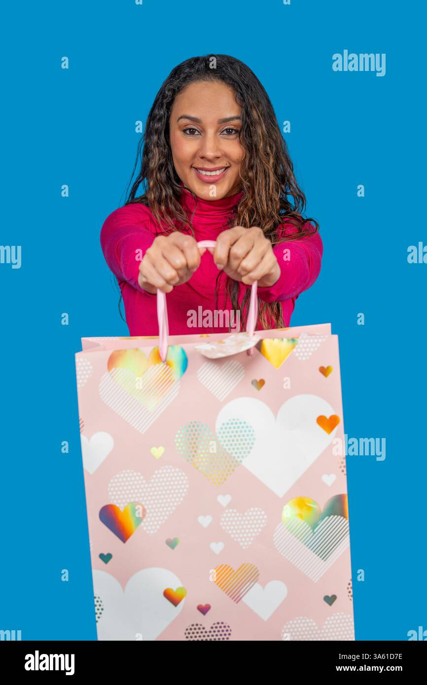 Donna sorridente che mostra una shopping bag rosa con il cuore, pronta per san valentino o per un'occasione speciale Foto Stock