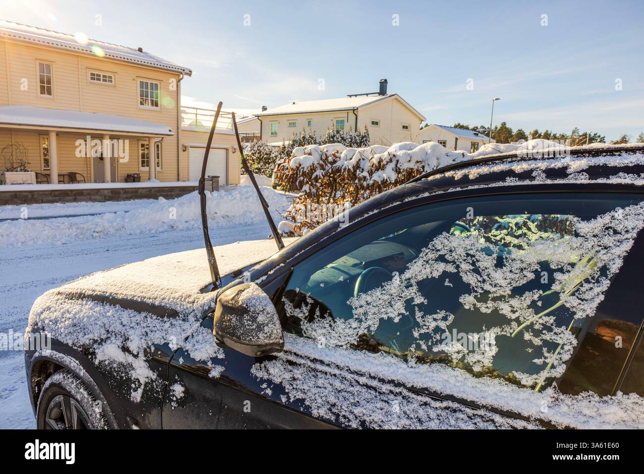 Auto nera con tergicristalli sollevati ricoperti di neve parcheggiata nel vialetto della villa nelle soleggiate giornate invernali. Foto Stock