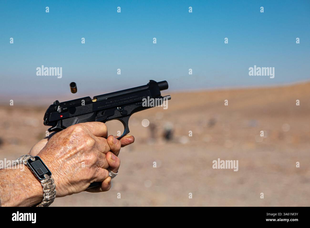 Un involucro esaurito viene espulso mentre un uomo spara una pistola semi-automatica nera. Foto Stock