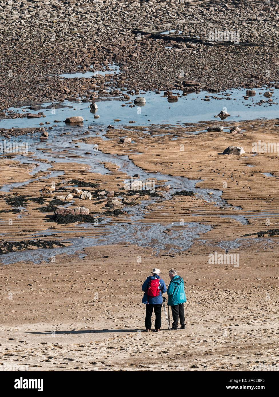La coppia senior consulta la mappa sulla spiaggia vestita con abiti da passeggio. Foto Stock