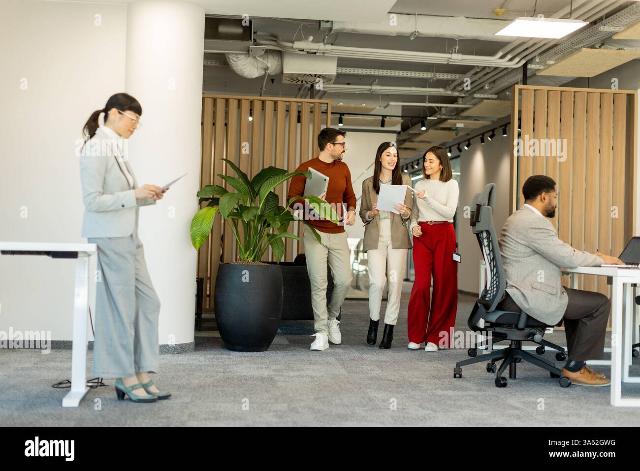 Un gruppo di professionisti si impegna in discussioni vivaci durante la revisione dei documenti, incarnando il lavoro di squadra e la creatività in un ambiente di lavoro luminoso e contemporaneo Foto Stock