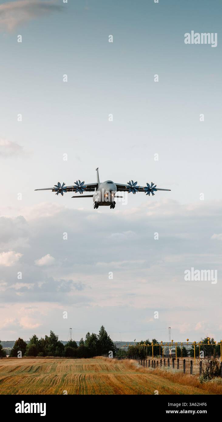 Immagine verticale del velivolo da carico grigio che atterra al tramonto: AN-70 che scende prima del touchdown, campo agricolo, sistema di illuminazione di avvicinamento nella parte posteriore. Foto Stock