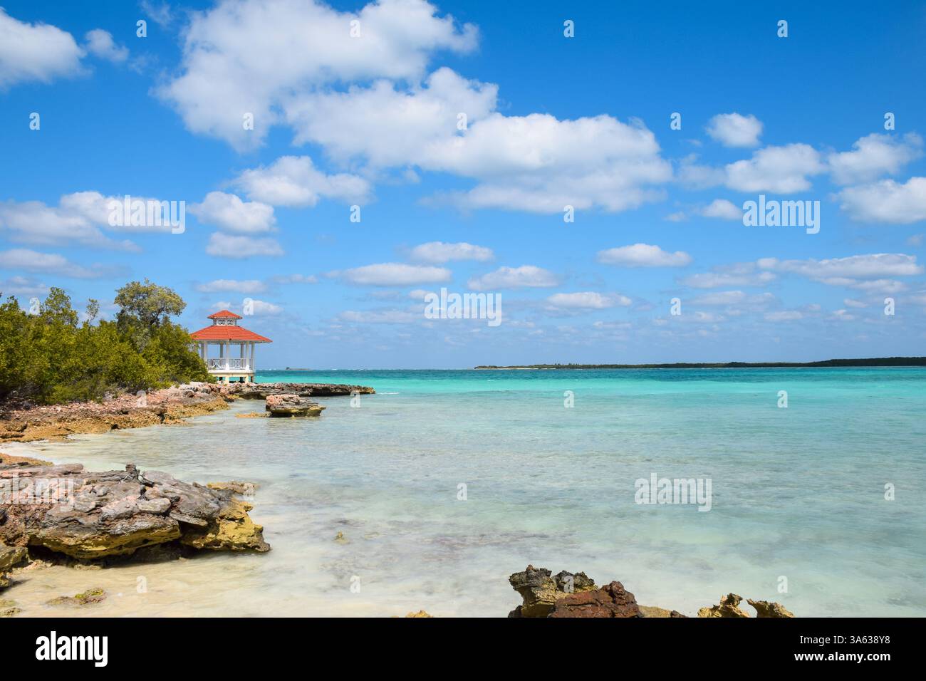 Splendida spiaggia rocciosa dell'oceano tropicale con acqua blu turqoiuse e gazebo in lontananza Foto Stock
