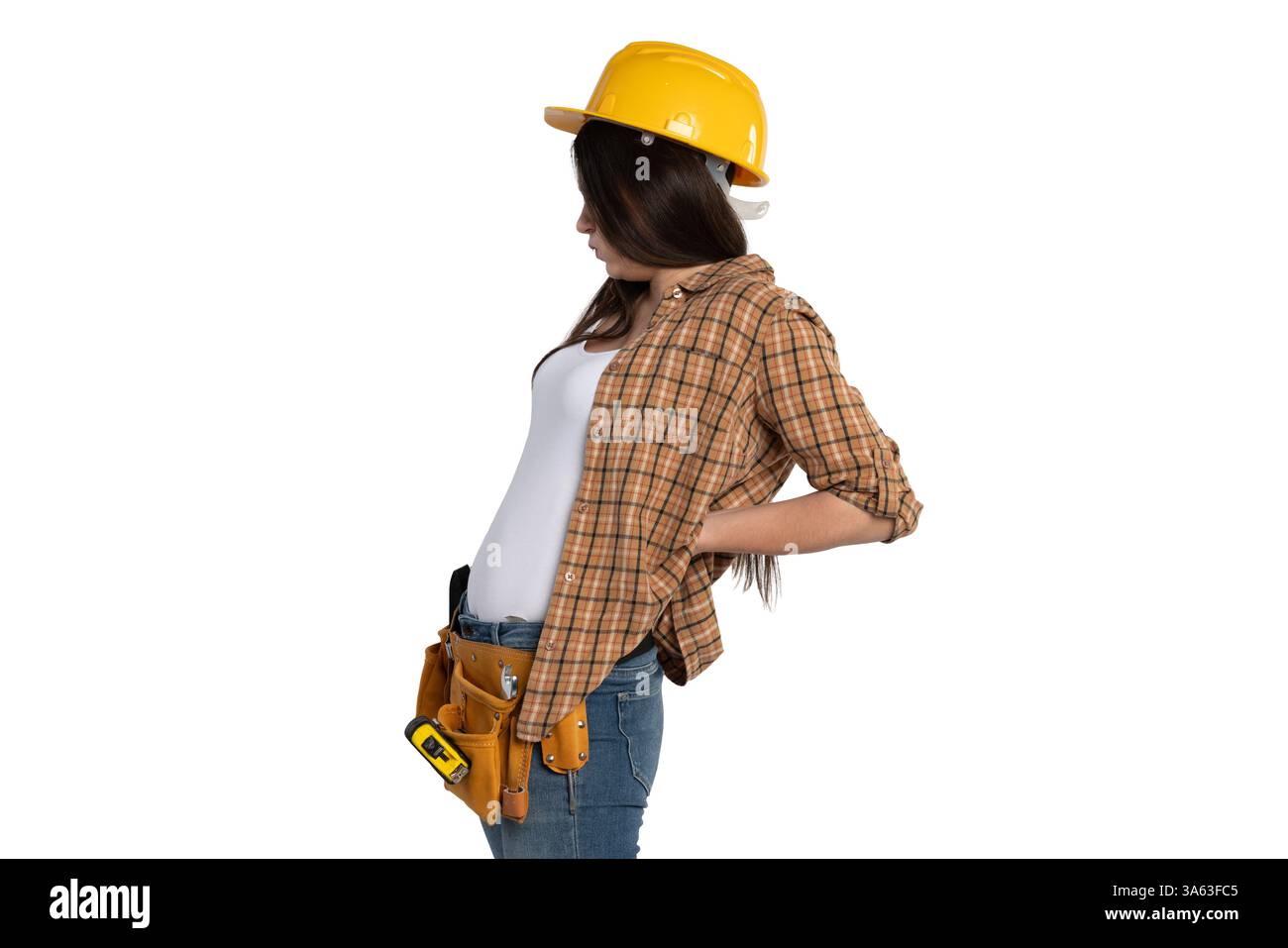Una lavoratrice edile che indossa un elmetto giallo e una cintura portautensili le regge la parte inferiore della schiena in disagio. Sembra soffrire di problemi di lavoro Foto Stock