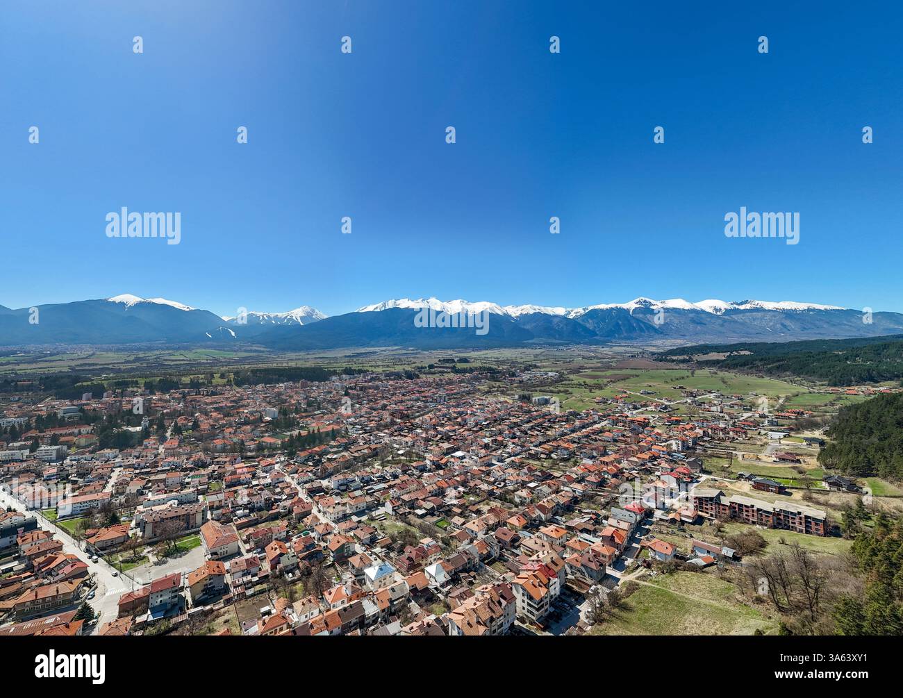 Vista aerea della città di Razlog in Bulgaria, con le montagne innevate di Pirin e il cielo azzurro, durante una splendida giornata di primavera Foto Stock