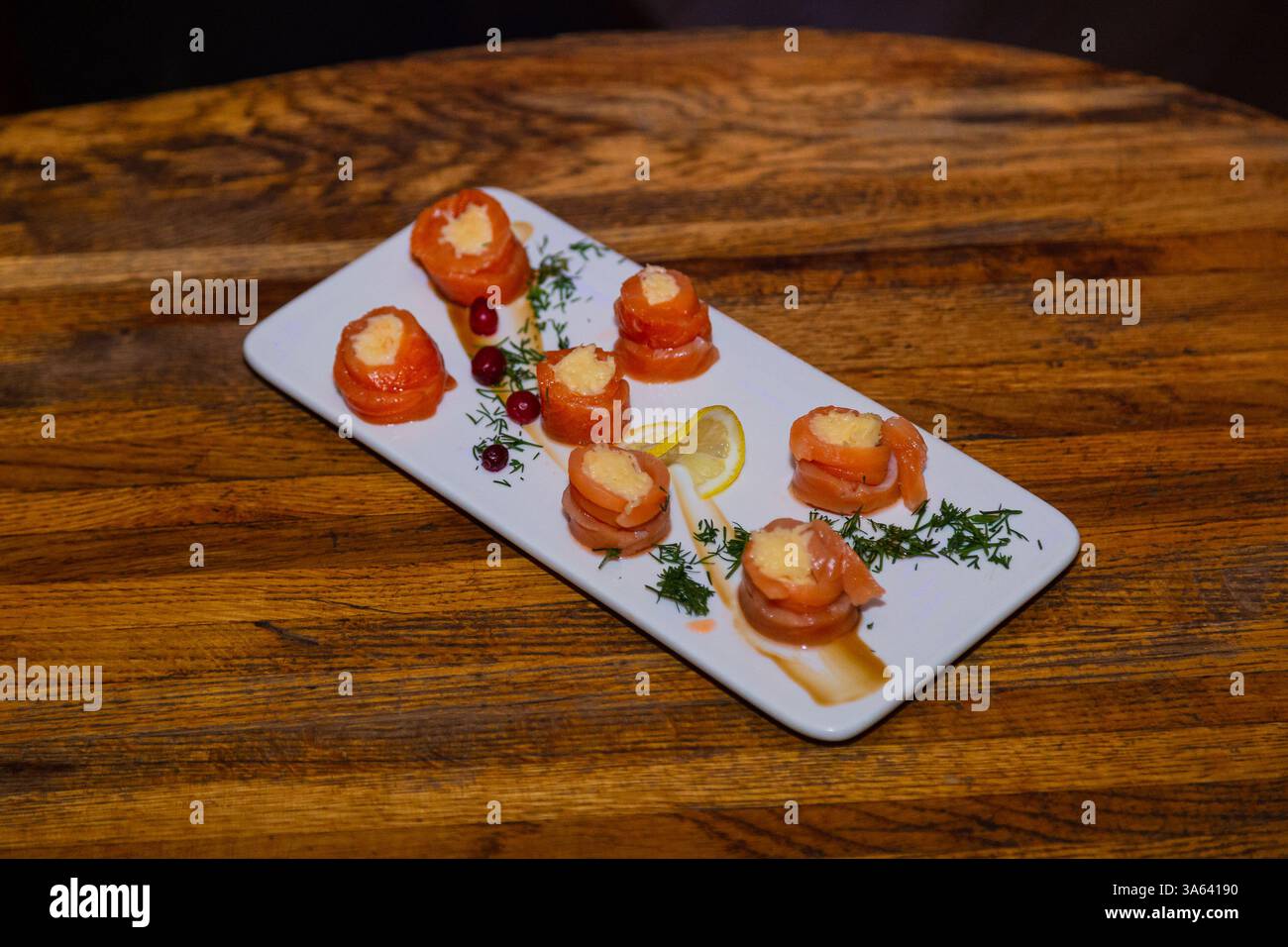 Appetitosi involtini di pesce rosso con ripieno all'interno su un piatto bianco e un tavolo di legno in un ristorante. Cibo gustoso Foto Stock