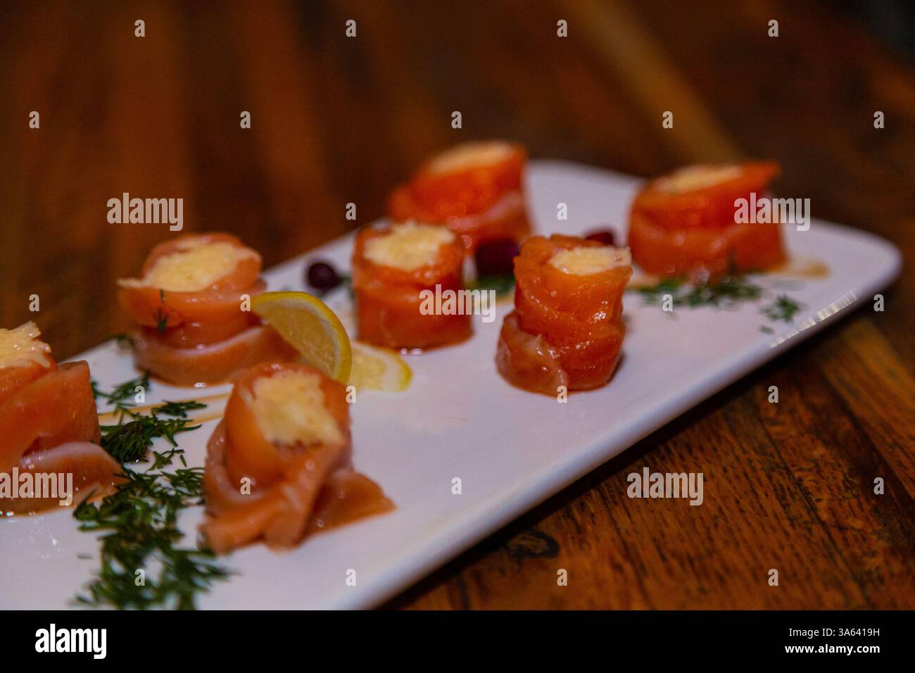 Appetitosi involtini di pesce rosso con ripieno all'interno su un piatto bianco e un tavolo di legno in un ristorante. Cibo delizioso a base di pesce Foto Stock