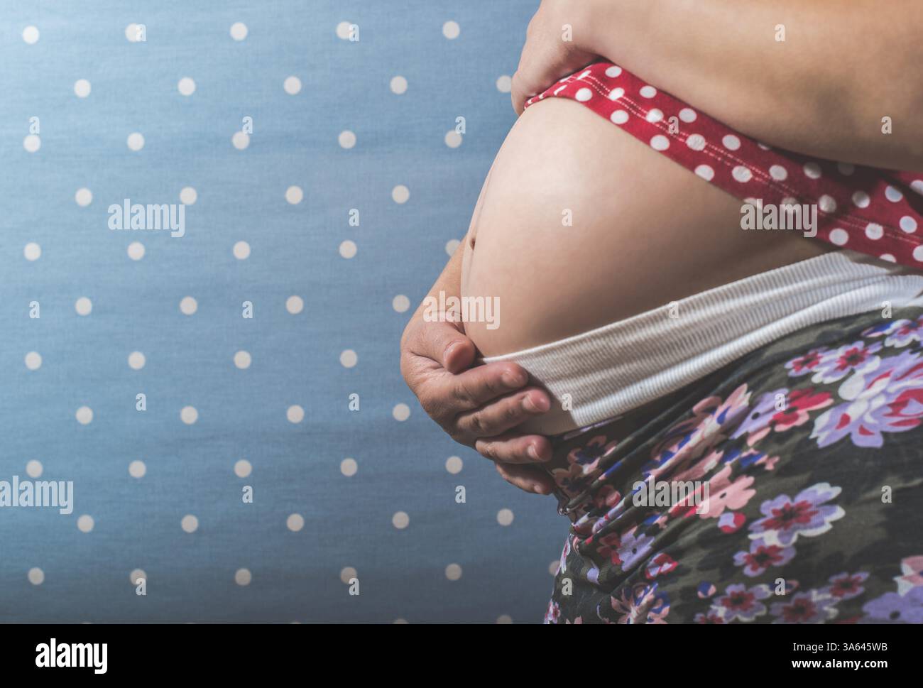 Donna incinta mostra il suo ventre. Sfondo blu Foto Stock