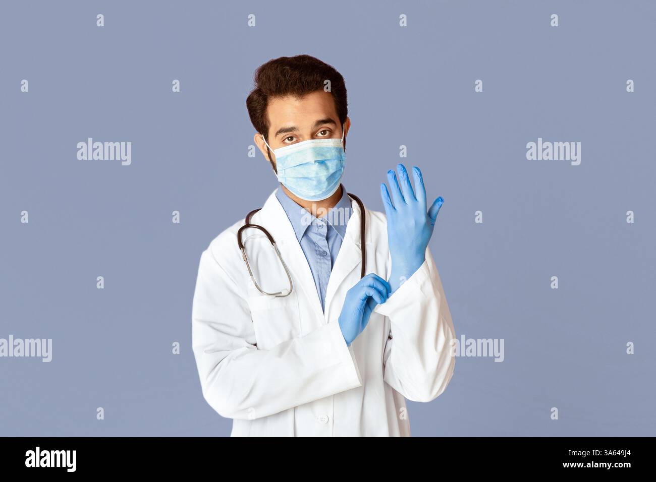 Protezione contro le malattie virali. Medico indiano che indossa maschera medica, camice da laboratorio e guanti di gomma su sfondo viola Foto Stock