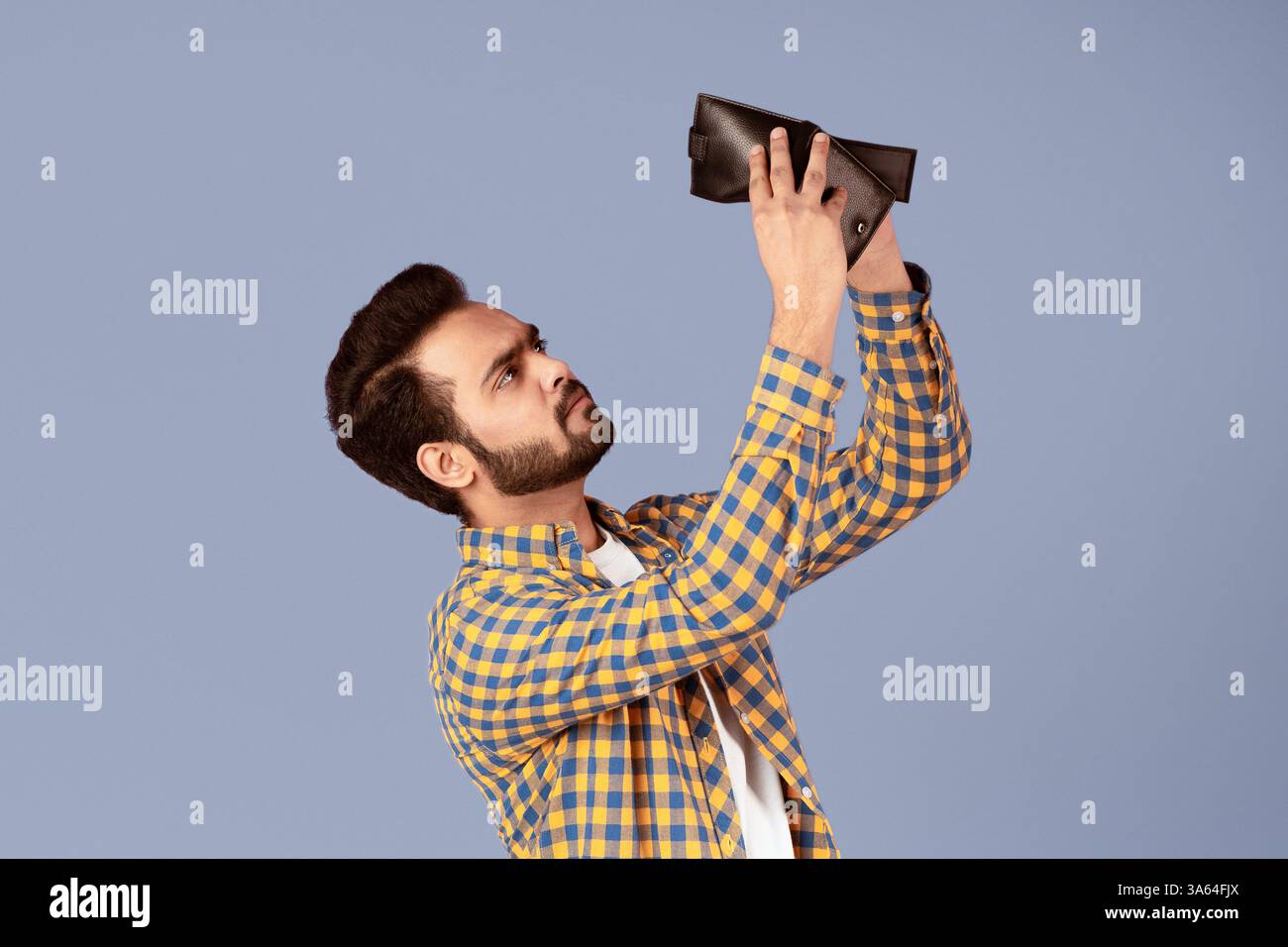 Concetto di crisi economica. Un ragazzo indiano sconvolto con un portafoglio vuoto su sfondo viola Foto Stock