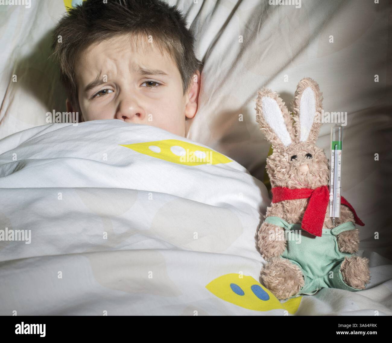 Bambino malato a letto con orsacchiotto. Misurazione della temperatura con un termometro Foto Stock