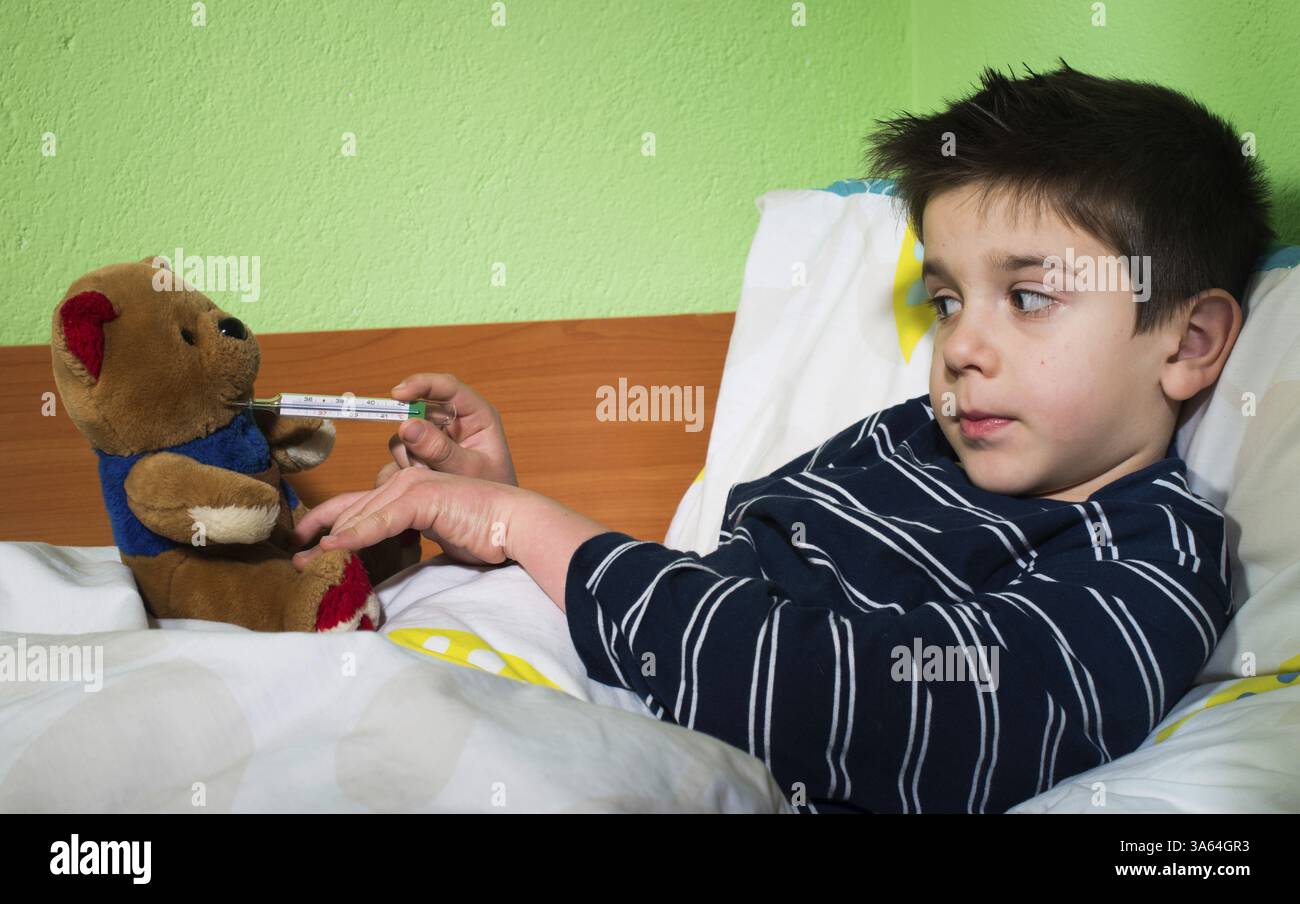 Bambino malato a letto con orsacchiotto. Misurazione della temperatura con un termometro Foto Stock