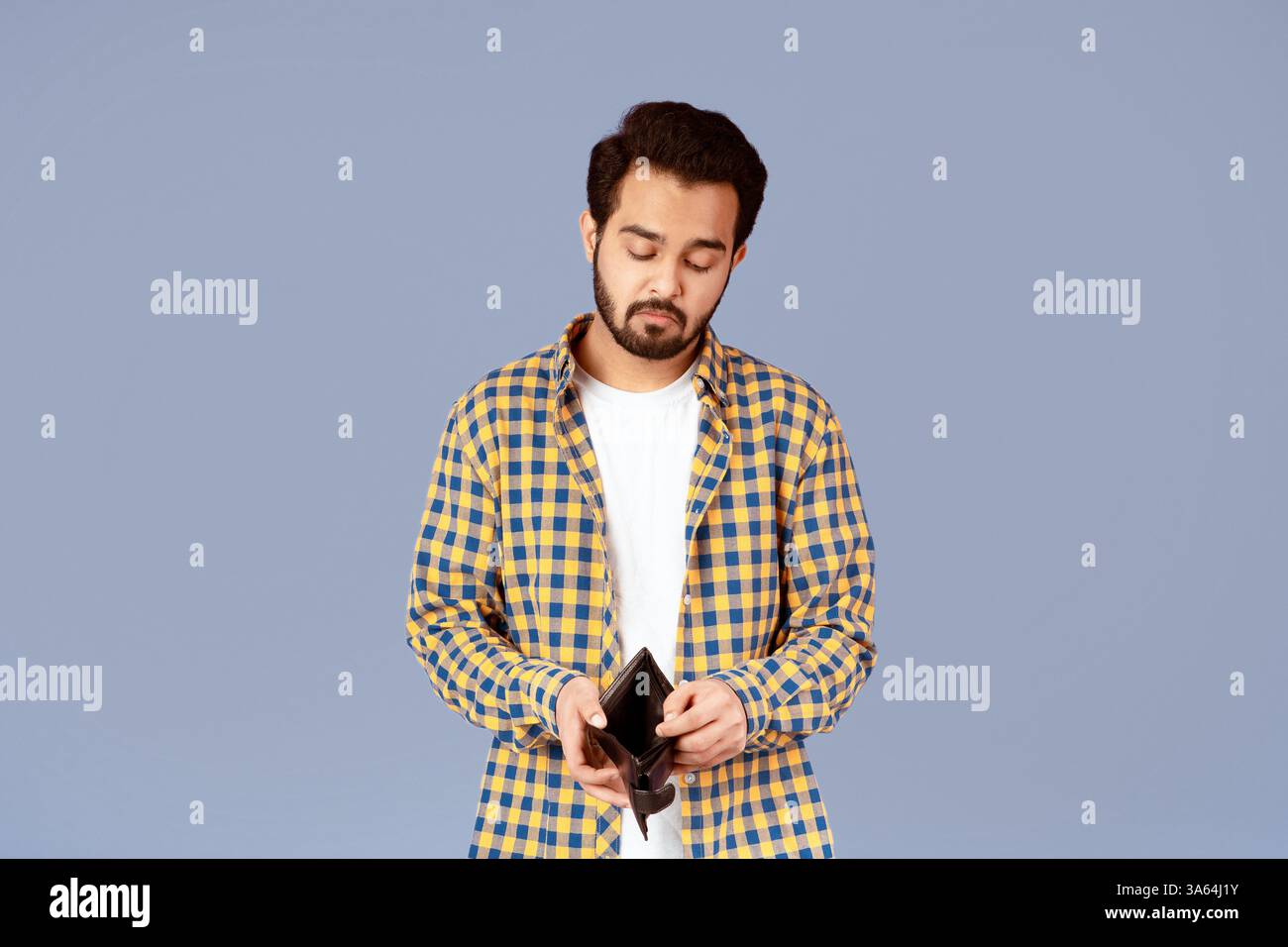 Crisi economica. Insoddisfatto ragazzo indiano che guarda nel portafoglio vuoto su sfondo viola Foto Stock