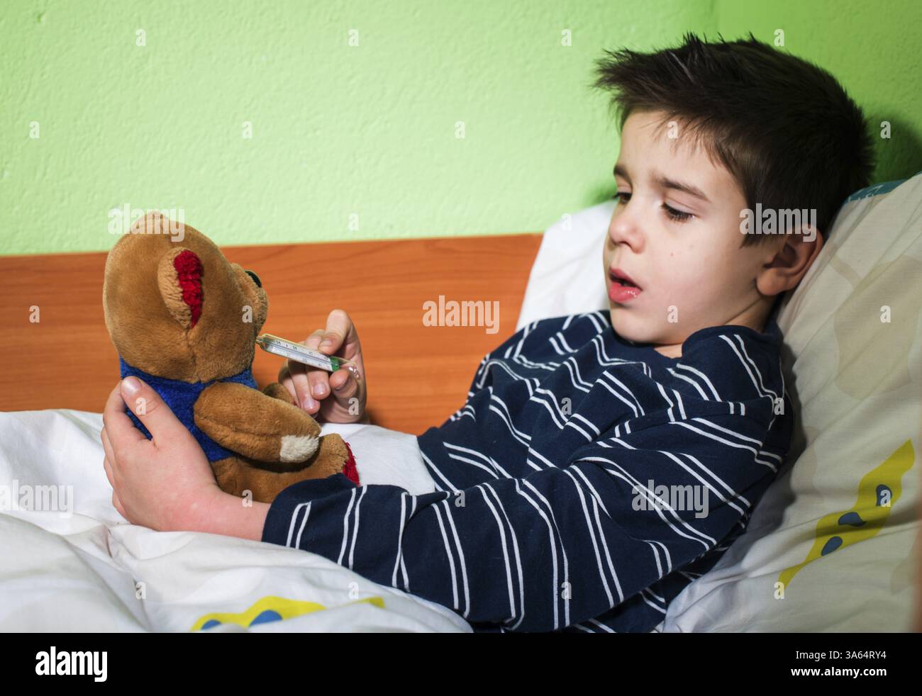Bambino malato a letto con orsacchiotto. Misurazione della temperatura con un termometro Foto Stock