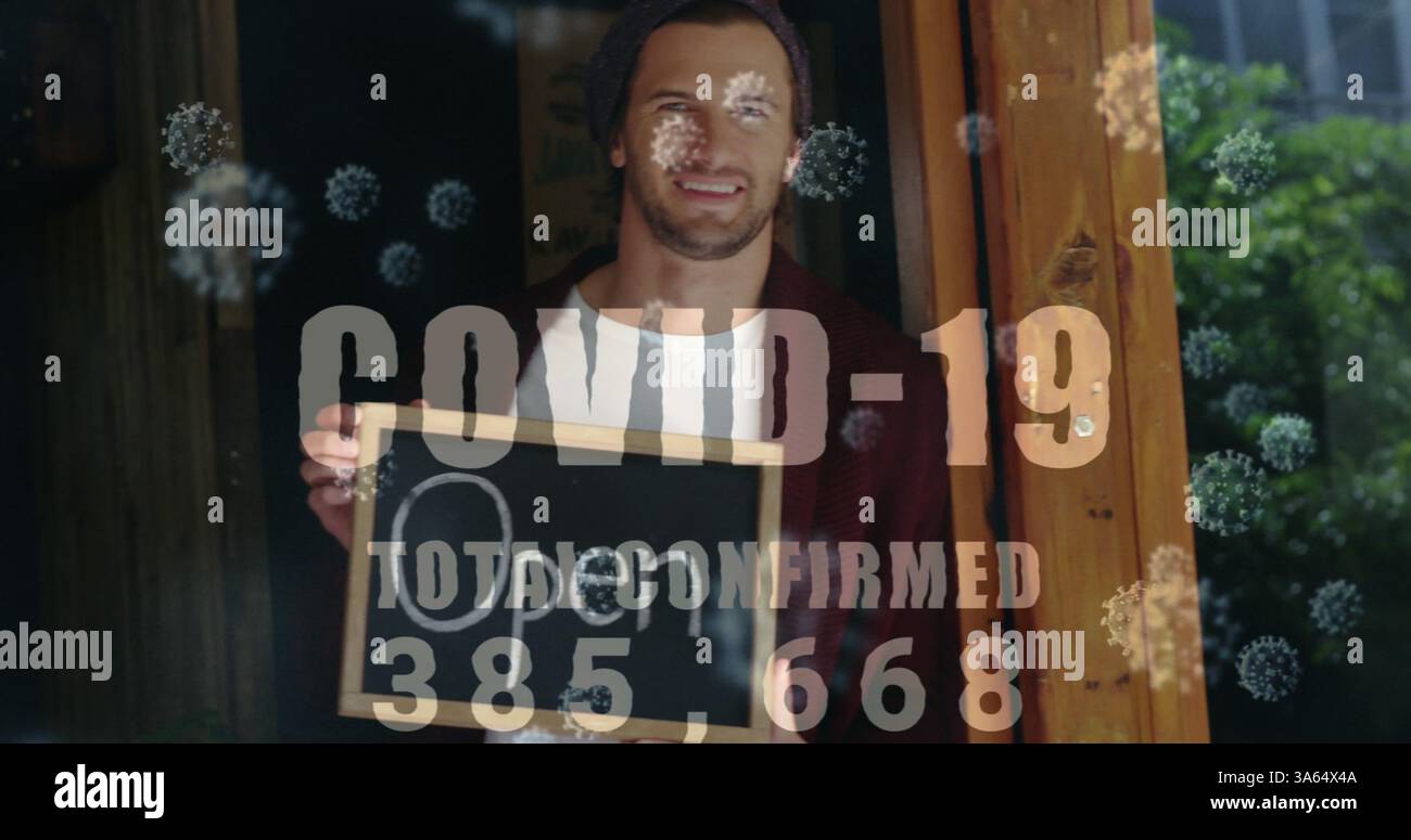 Proprietario di una piccola impresa con un cartello aperto, sorridendo attraverso la finestra durante la pandemia Foto Stock