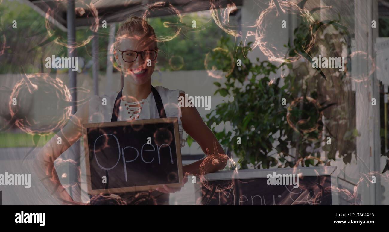 Donna sorridente che tiene in mano il cartello aperto al bar all'aperto, pronta ad accogliere i clienti Foto Stock