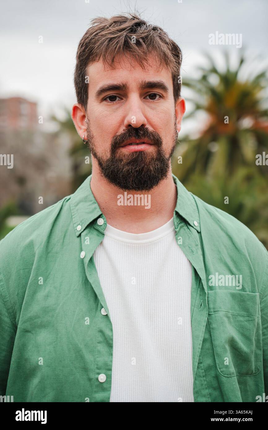 Ritratto verticale di un giovane con la barba che guarda direttamente la fotocamera, trasuda sicurezza e forza. La sua intensa espressione cattura lo spettatore, rivelando livelli di personalità e profondità. Foto di alta qualità Foto Stock