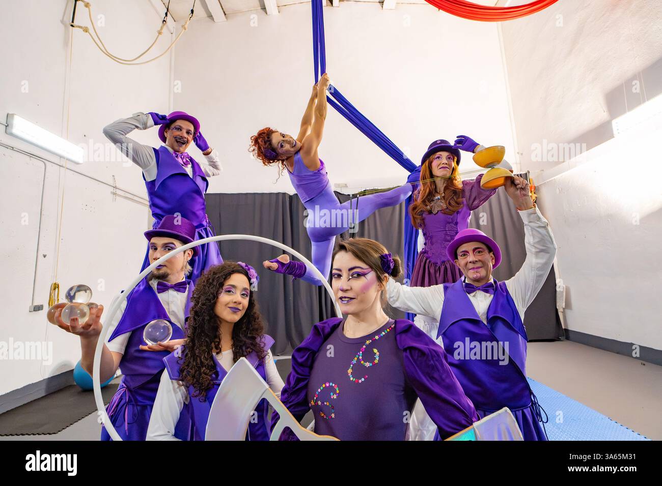 Gruppo di artisti del circo che indossano costumi viola che si mettono insieme in posa in una struttura di allenamento, giocolano, bilanciano e fanno acrobazie aeree Foto Stock Gruppo di artisti del circo che indossano costumi viola che si mettono insieme in posa in una struttura di allenamento, giocolano, bilanciano e fanno acrobazie aeree Foto Stock