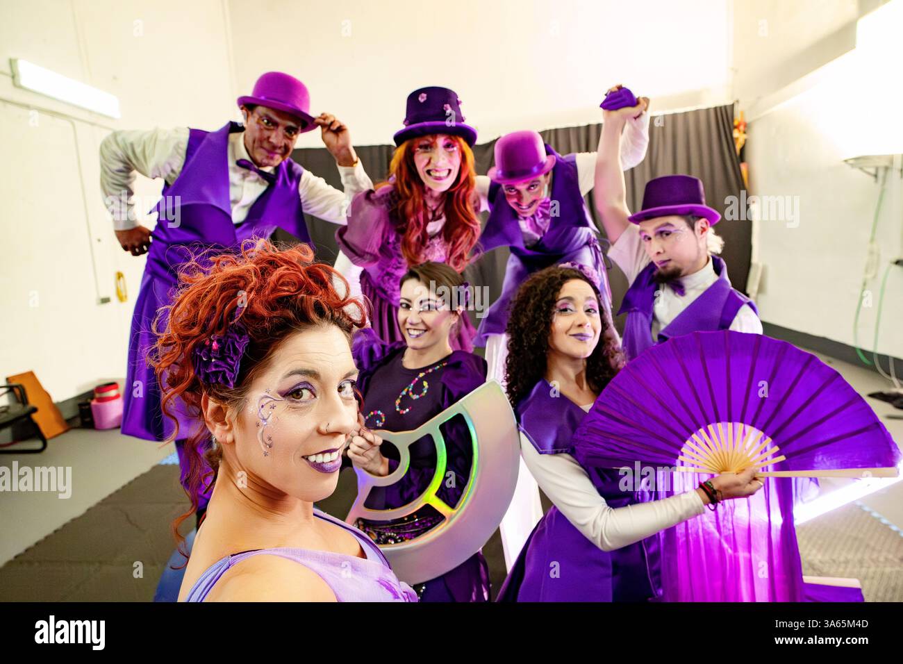 Gruppo di artisti circensi sorridenti che indossano costumi viola e tengono in mano vari accessori, mettendosi insieme per una foto di gruppo Foto Stock Gruppo di artisti circensi sorridenti che indossano costumi viola e tengono in mano vari accessori, mettendosi insieme per una foto di gruppo Foto Stock