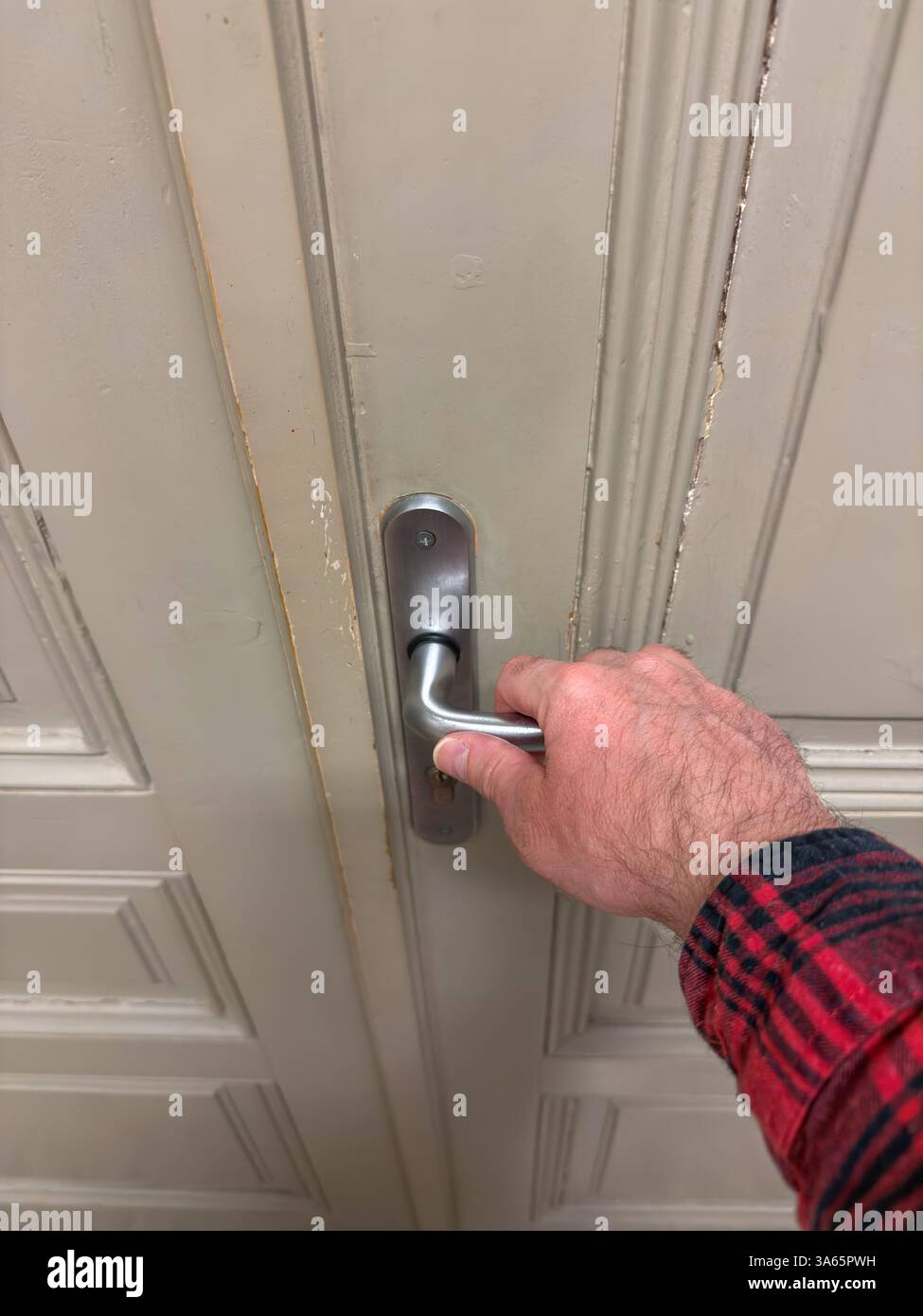 Primo piano della mano di una persona che afferra una maniglia di porta argentata su una porta di classe usurata, suggerendo l'azione di entrare o uscire da uno spazio educativo. Foto Stock