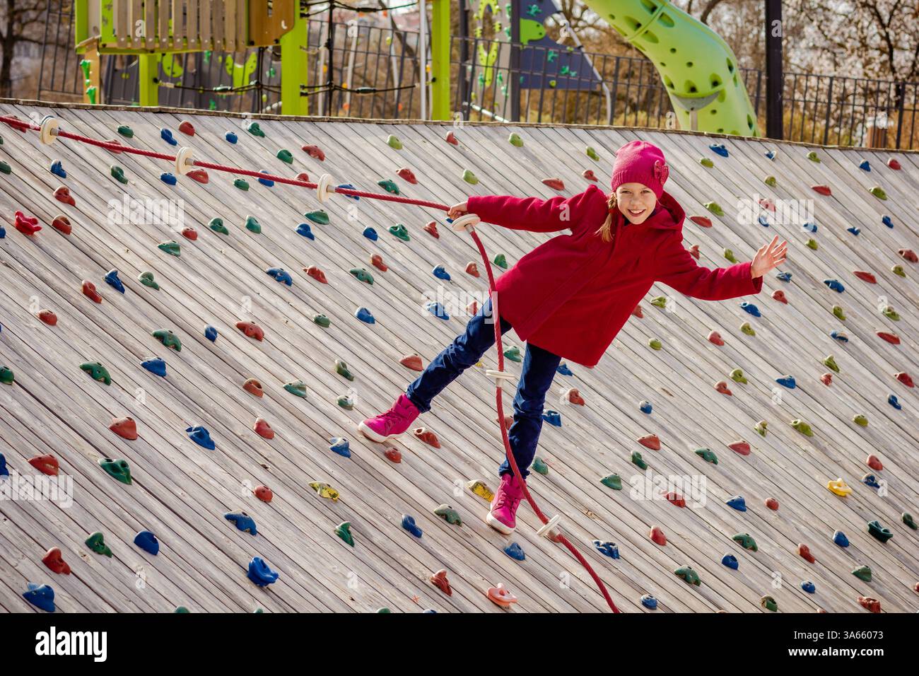 Bambino felice che si arrampica su una parete di roccia artificiale nel parco giochi Foto Stock