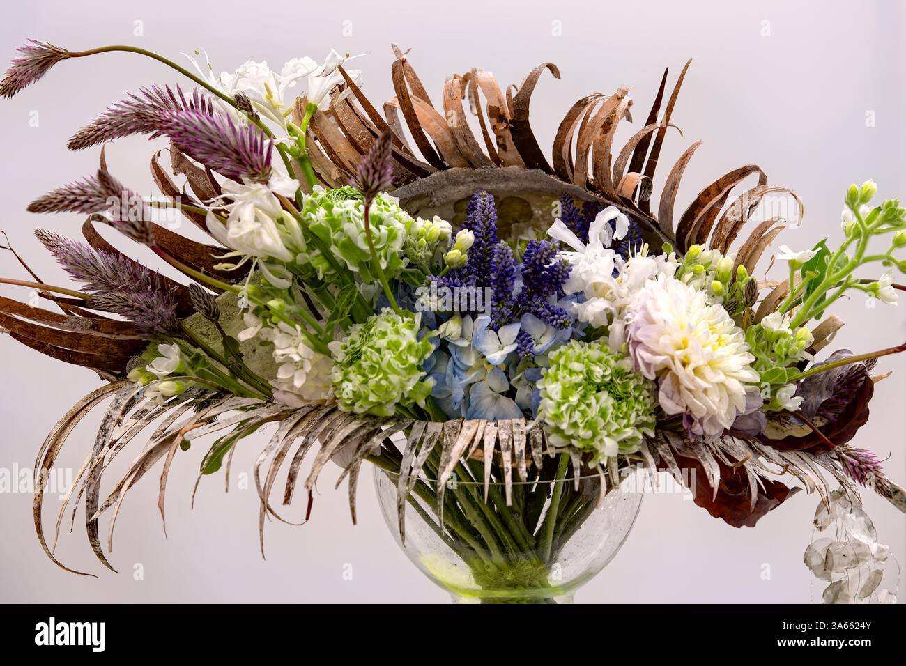 Splendida composizione floreale con fiori ed erbe verdi, blu e bianche. Bouquet autunnale in vaso di vetro su sfondo bianco. Foto Stock