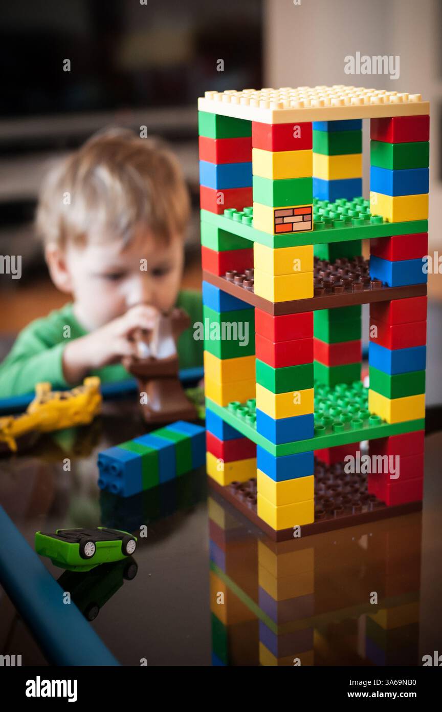 Un bambino è impegnato nel gioco creativo costruendo una torre vibrante utilizzando mattoni. L'atmosfera gioiosa cattura un momento di immaginazione Foto Stock