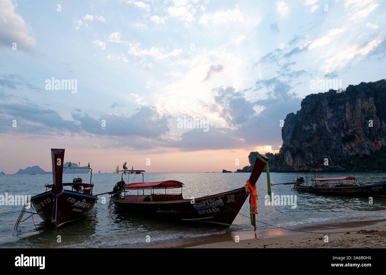 Le barche a coda lunga riposano sulla spiaggia di Tonsai al tramonto, incorniciate da scogliere calcaree e cieli pastello Foto Stock