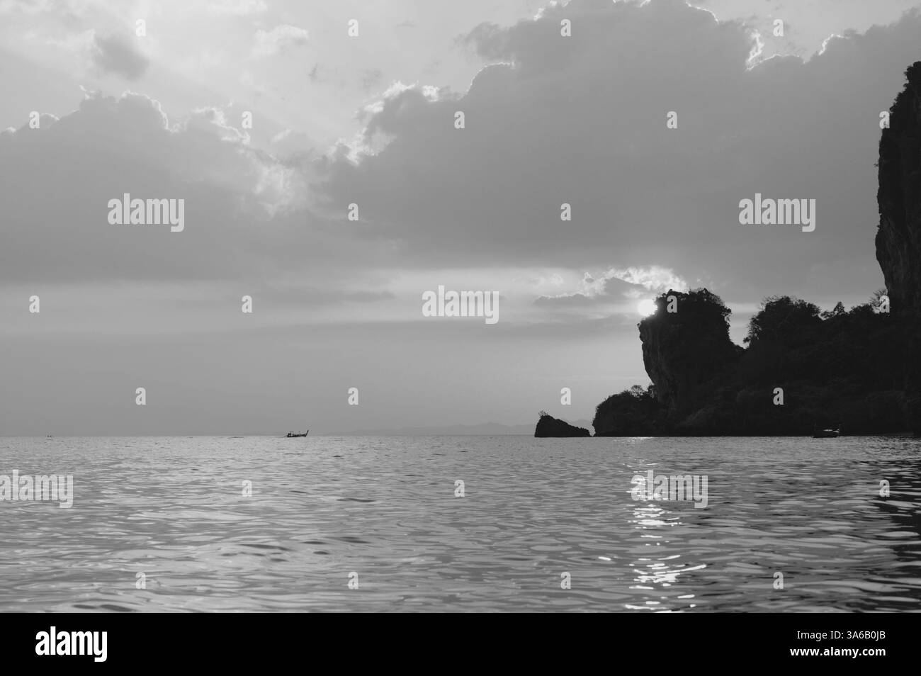 La luce del sole si irrompe dietro le scogliere calcaree al largo di Tonsai Beach, gettando riflessi sulle acque calme in questo paesaggio marino bianco e nero Foto Stock