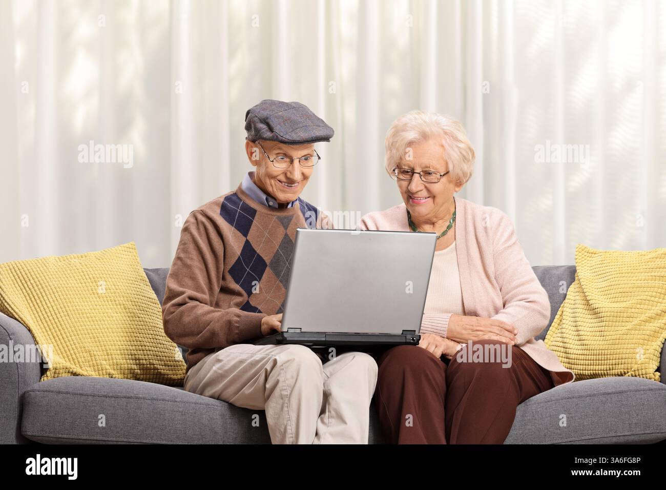 Coppia di anziani seduta su un divano e con un computer portatile Foto Stock