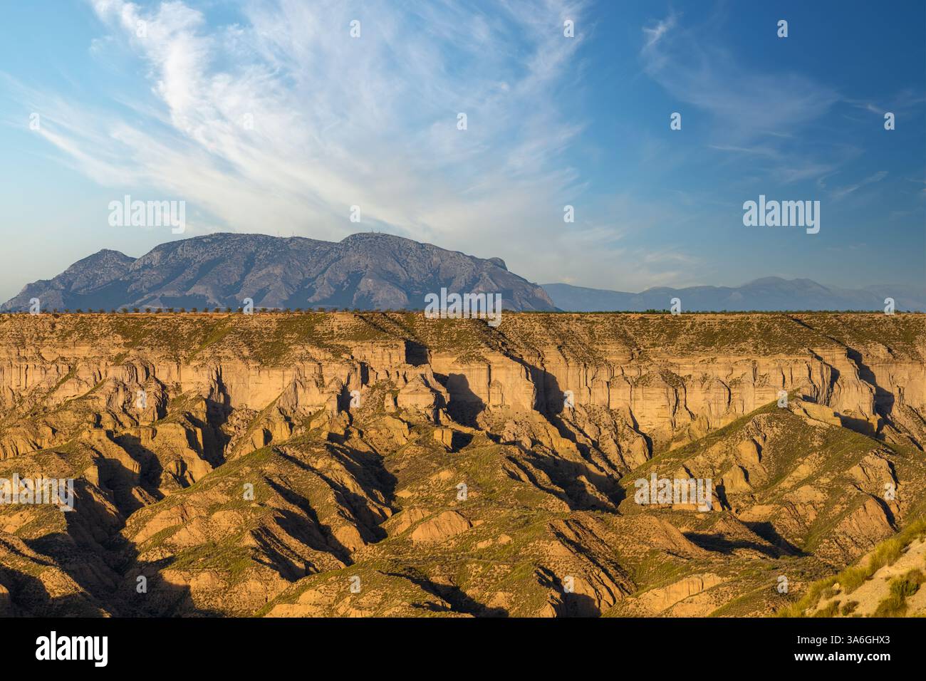Una stupenda catena montuosa incombe sui canyon profondamente erosi sotto un vasto cielo azzurro con nuvole mostruose Foto Stock