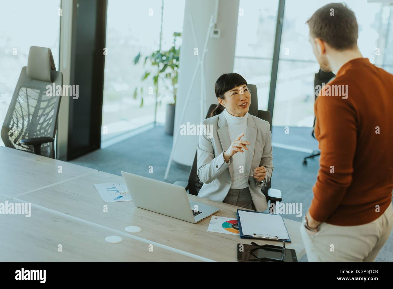 Due colleghi si impegnano in una vivace discussione in un ufficio contemporaneo, scambiando idee e approfondimenti mentre un altro membro del team lavora concentrato sulla ba Foto Stock