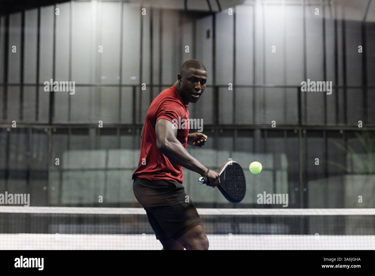 Atletico che gioca a tennis del padel, concentrandosi sul colpire la palla con la racchetta Foto Stock