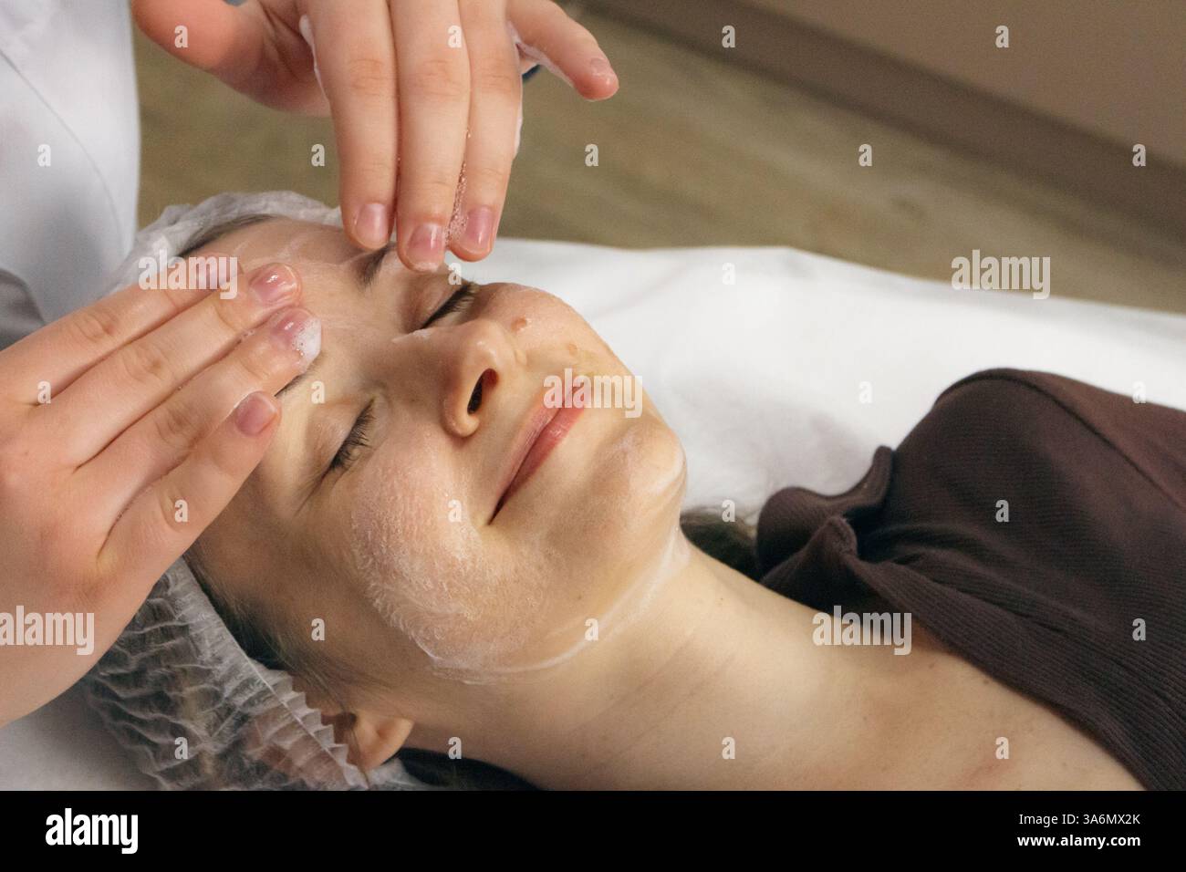 Pulizia della schiuma e massaggio viso nel salone di bellezza. Donna sorridente che si rilassa con un massaggio anti-età. Procedura di benessere. Trattamento per la cura della pelle. Foto Stock